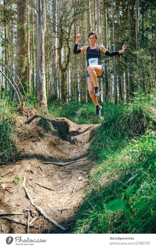 Springende Frau, die am Trail Race teilnimmt. Lifestyle Sport Mensch Erwachsene Natur Baum Wald Wege & Pfade Fitness springen authentisch Geschwindigkeit