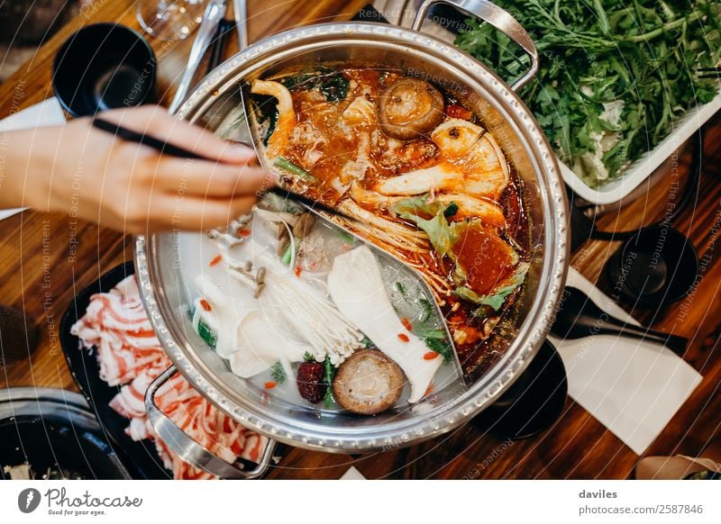 Koreanisches Eintopfgericht, von oben betrachtet, und eine Hand nimmt mit Stäbchen Essen daraus. Lebensmittel Fleisch Gemüse Suppe schmoren Abendessen