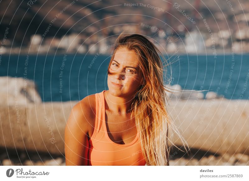 Schöne Frau in Sportkleidung, die bei Sonnenuntergang auf einer Betonmauer im Freien sitzt. Lifestyle schön Körper Freizeit & Hobby Meer Fitness Sport-Training