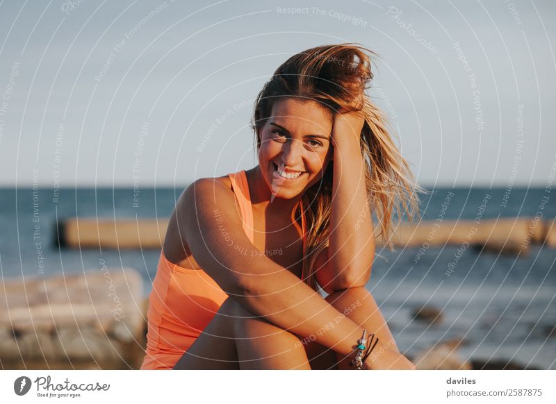 Schöne Frau in Sportkleidung, die bei Sonnenuntergang auf einer Betonmauer im Freien sitzt. Lifestyle Freude schön Körper Wellness Erholung Meer Fitness