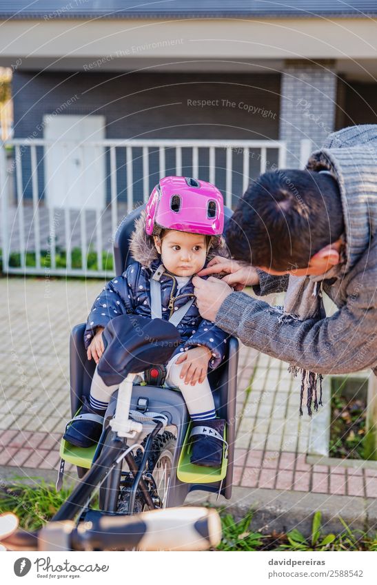Vater schließt Helm zu ihrer Tochter, die im Fahrradsattel sitzt. Lifestyle Freizeit & Hobby Ferien & Urlaub & Reisen Ausflug Stuhl Fahrradfahren Kind Baby