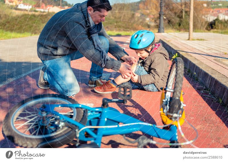 Vater legt dem Sohn ein Gipsband über die Knieverletzung. Medikament Sport Fahrradfahren Kind Junge Mann Erwachsene Band Straße Wege & Pfade schreien