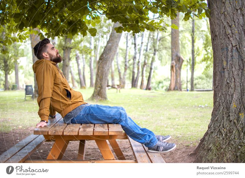 Mann sitzt in einem Park, auf einem Picknicktisch. Lifestyle Wellness Wohlgefühl Erholung Ferien & Urlaub & Reisen Freiheit Junger Mann Jugendliche Körper 1