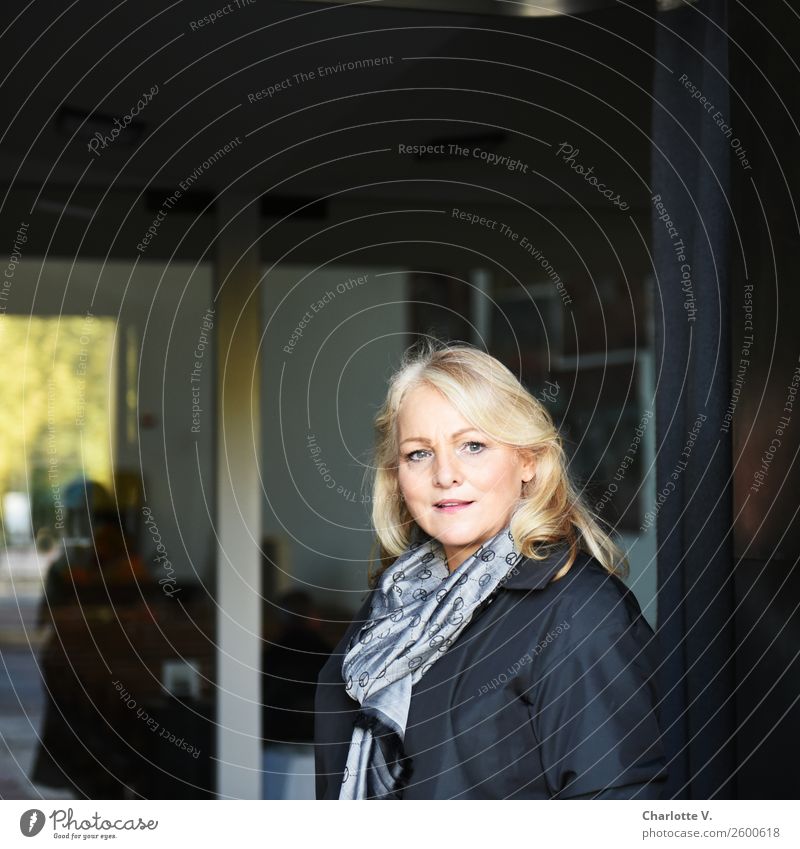 Komm mit! Mensch feminin Frau Erwachsene Weiblicher Senior 1 45-60 Jahre Fenster Eingang Schal blond langhaarig Glas Kommunizieren Lächeln leuchten Blick stehen