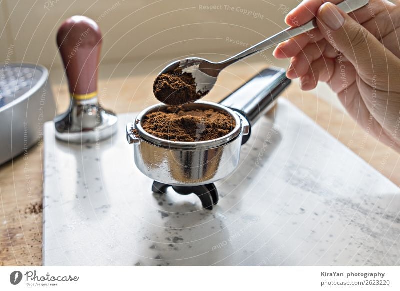 Weibliche Hand legt frisch gemahlenen Kaffee in den Portafilter. Frühstück Getränk Espresso Löffel Küche Holz Stahl dunkel heiß braun grün schwarz weiß