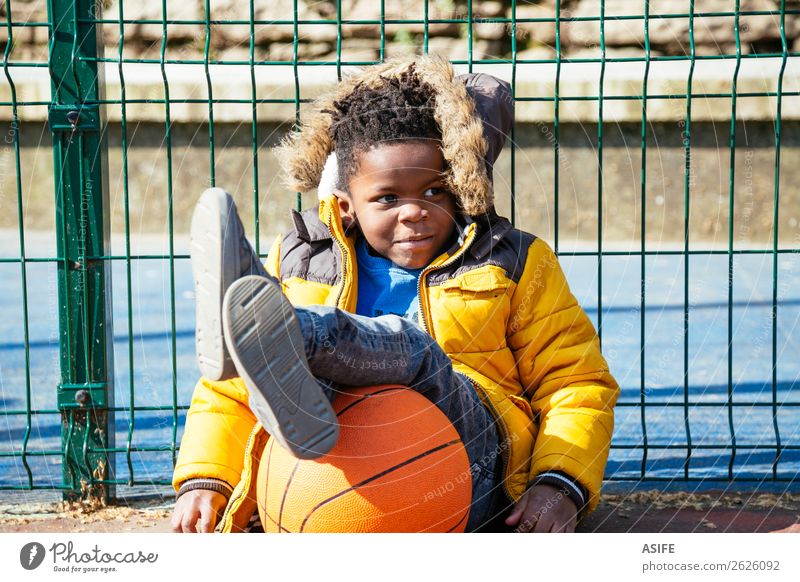 Lustiger kleiner Junge ruht sich aus, nachdem er Basketball gespielt hat. Freude Glück Erholung Freizeit & Hobby Spielen Winter Sport Kind Schule Kindheit