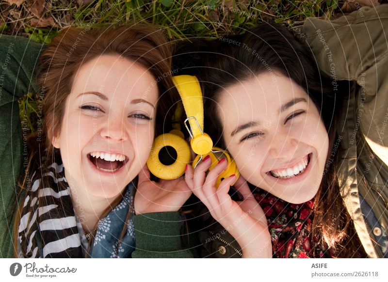 Zwei glückliche Teenager-Mädchen liegen auf dem Gras und teilen Kopfhörer, um Musik zu hören Freude schön Winter Headset Mensch Frau Erwachsene Freundschaft