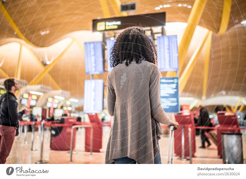 Black Woman betrachtet das Fahrplanauskunftstafel im Flughafen mit einem Koffer. Zeitplanung Anzeige Panel Mensch Etage Holzplatte international Frau