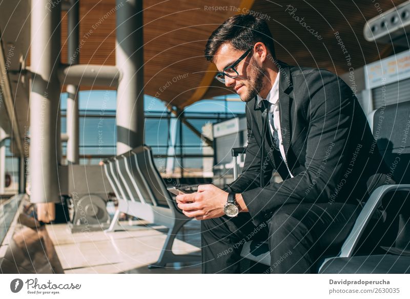 Junger Geschäftsmann am Telefon mit dem Koffer am Flughafen, der auf den Flug wartet. Mann Ferien & Urlaub & Reisen Mobile Mitteilung Technik & Technologie