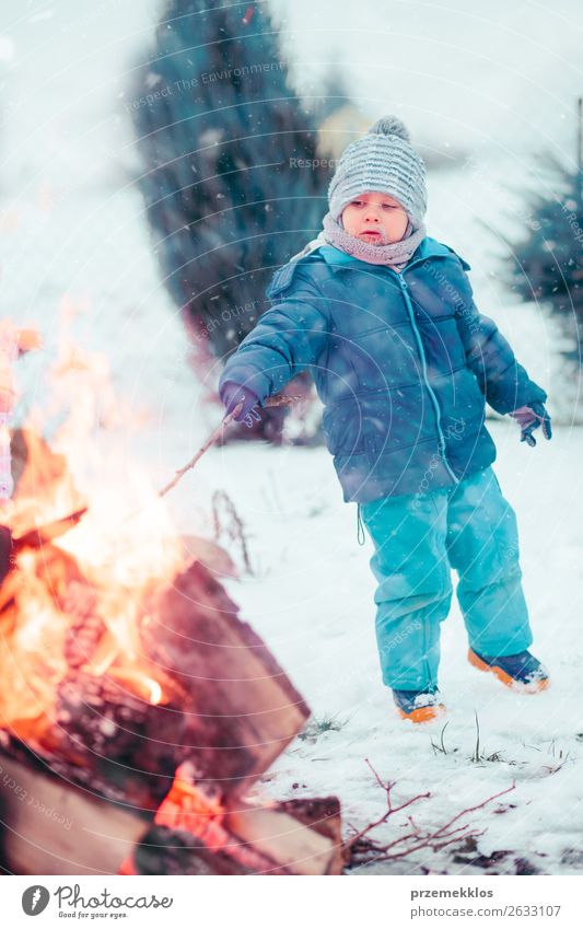 Junge spielt im Winter am Lagerfeuer im Freien einen Stock. Lifestyle Freude Glück Freizeit & Hobby Schnee Garten Kind Mensch 1 3-8 Jahre Kindheit Schneefall