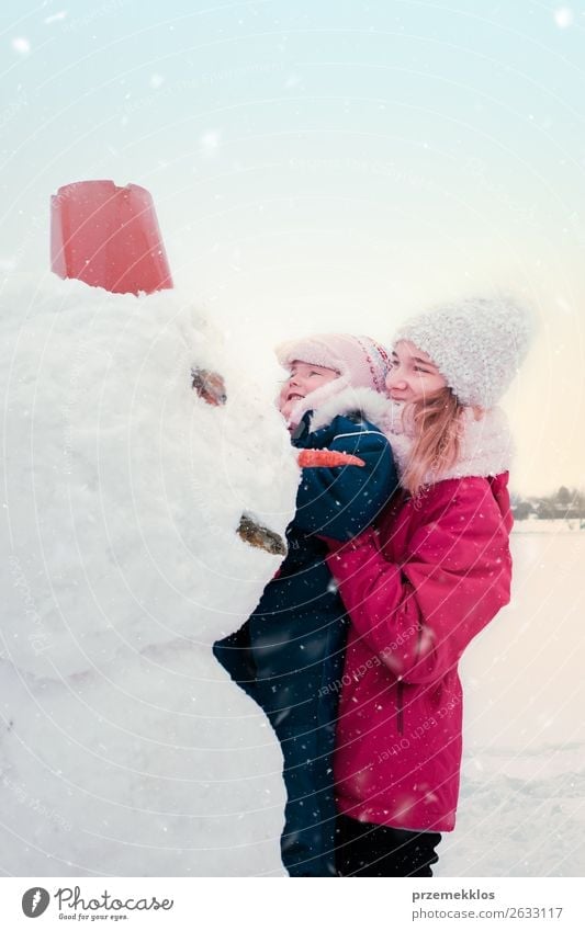 Mädchen und ihre kleine Schwester machen einen Schneemann. Lifestyle Freude Glück Winter Winterurlaub Kind Mensch Junge Frau Jugendliche Erwachsene