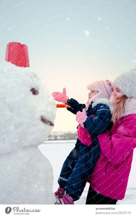 Mädchen und ihre kleine Schwester machen einen Schneemann. Lifestyle Freude Glück Winter Winterurlaub Kind Mensch Junge Frau Jugendliche
