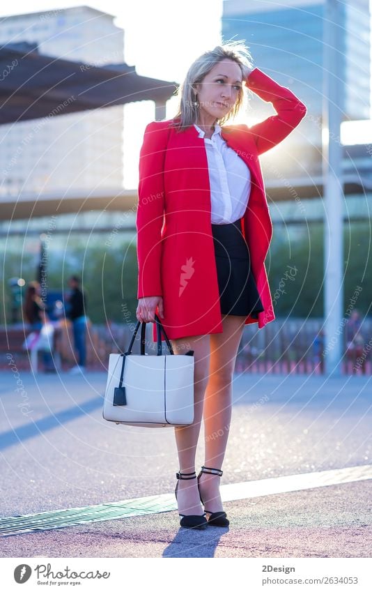 Elegante blonde Frau, die auf der Straße steht und eine rote Jacke trägt. elegant Stil schön Mensch feminin Erwachsene Mode Hemd Rock Schuhe Damenschuhe stehen