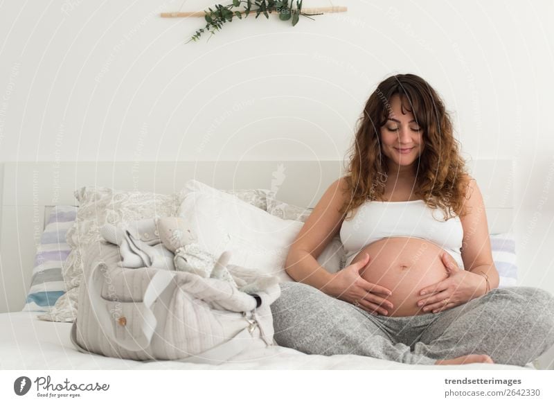 Glückliche schwangere Frau, die zu Hause sitzt und ihren Bauch berührt Lifestyle schön Leben Freizeit & Hobby Sofa Mensch Baby Erwachsene Eltern Mutter