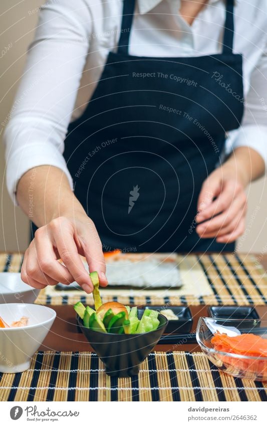 Koch hebt geschnittene Avocado auf, um Sushi zu machen. Meeresfrüchte Diät Restaurant Mensch Frau Erwachsene Hand frisch Küchenchef nehmen vorbereitend
