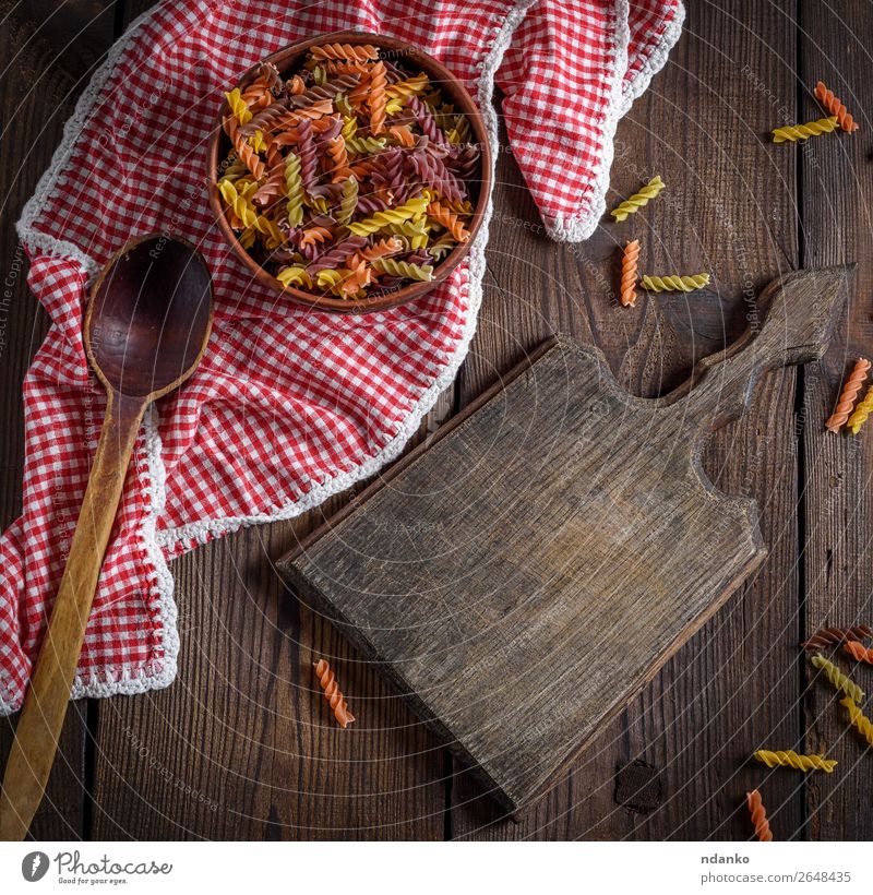 rohe Nudelnusilli auf einem braunen Holztisch Teigwaren Backwaren Ernährung Diät Schalen & Schüsseln Löffel Essen retro gelb rot Farbe Tradition farbenfroh