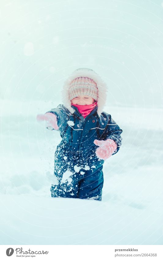 Fröhliches kleines Mädchen genießt den Schnee. Kind, das draußen spielt und im Winter bei Schneefall durch tiefen Schnee läuft. Kleinkind trägt dunkelblauen Schneeanzug