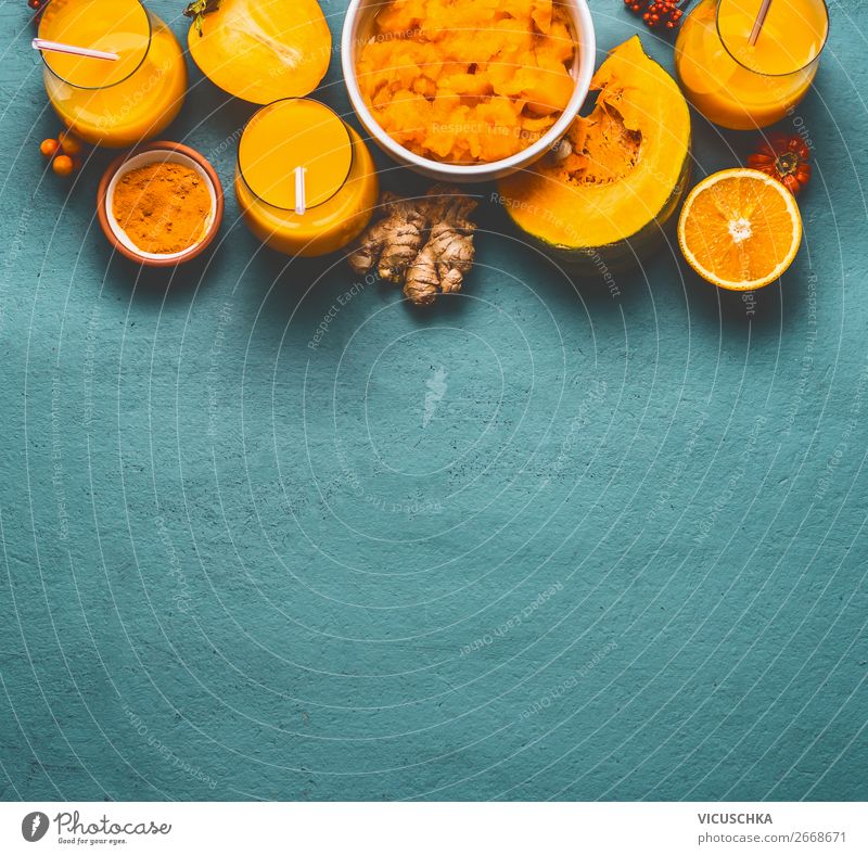 Gesunder Kürbis-Smoothie in Gläsern mit orangefarbenen Zutaten: Kaki, orangefarbene Früchte, Ingwer- und Kurkumapulver auf blauem Hintergrund, Ansicht von oben. Immunitätsförderndes Entgiftungsgetränk für die kalte Jahreszeit