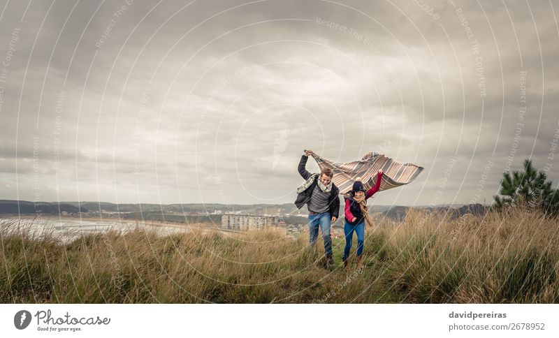 Junges Paar, das an einem windigen Tag im Freien mit Decke spielt. Lifestyle Freude Glück schön Spielen Meer Winter Berge u. Gebirge Frau Erwachsene Mann Natur