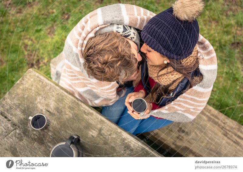 Junges Paar unter der Decke mit heißem Getränk, das sich im Freien küsst. Kaffee Tee Lifestyle Glück Winter Tisch Frau Erwachsene Mann Hand Natur Herbst Wind