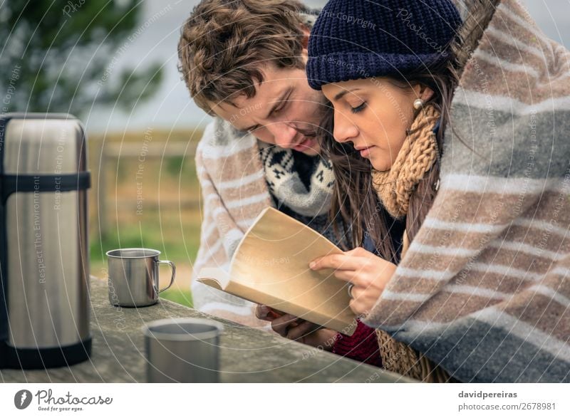 Junges Paar unter der Decke liest Buch im Freien an einem kalten Tag. Getränk Kaffee Tee Lifestyle lesen Abenteuer Winter Berge u. Gebirge Tisch Frau Erwachsene