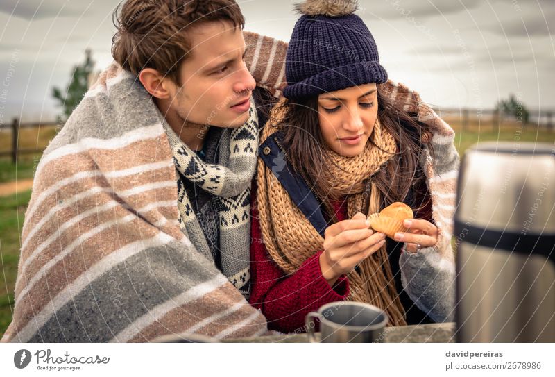 Junges schönes Paar unter Decke essen Muffin mit dunklen bewölkten Himmel auf dem Hintergrund Essen Getränk Kaffee Tee Lifestyle Glück Meer Winter Tisch Frau