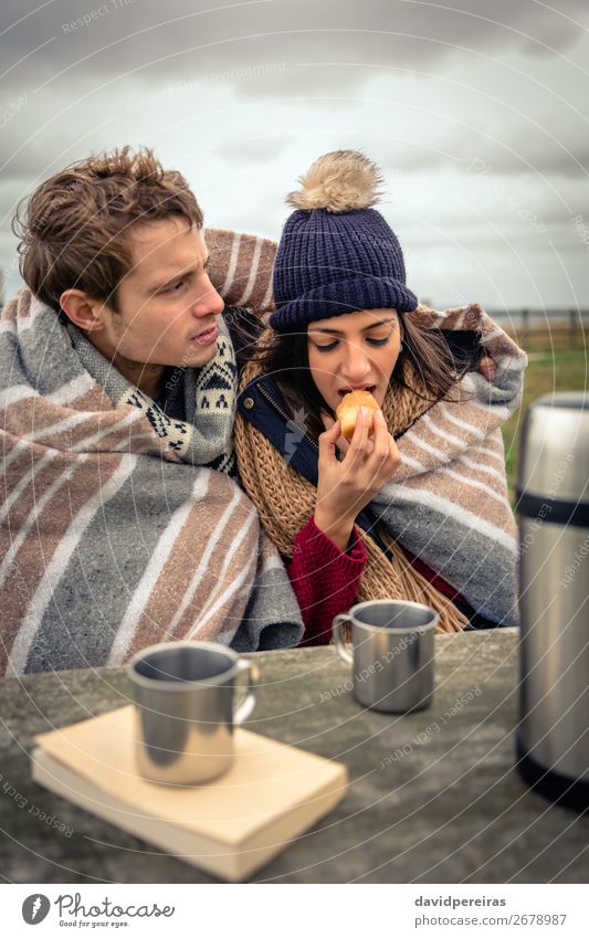 Junges Paar unter der Decke isst Muffin im Freien an einem kalten Tag. Essen Getränk Kaffee Tee Lifestyle Abenteuer Meer Winter Tisch Frau Erwachsene Mann Natur