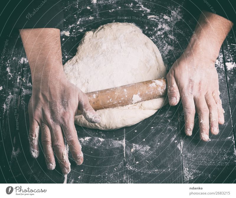 Chefkoch in einer schwarzen Tunika rollt einen Teig für eine runde Pizza. Teigwaren Backwaren Brot Ernährung Tisch Küche Mensch Mann Erwachsene Hand Holz machen
