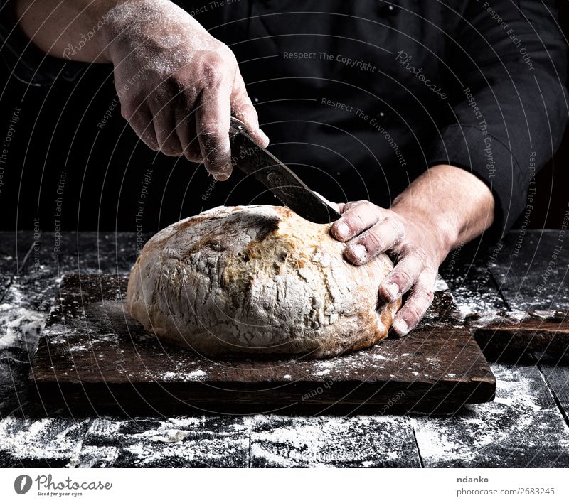 Mann schneidet mit einem Messer einen runden ganzen Laib. Brot Ernährung Tisch Küche Mensch Hand Finger Holz machen dunkel frisch braun schwarz weiß Tradition
