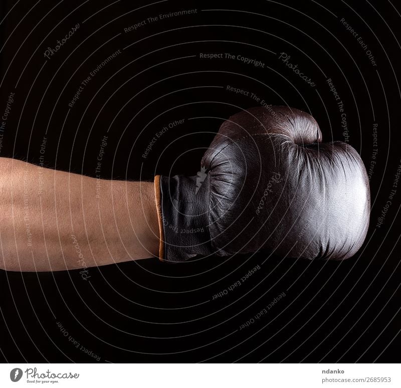 Hand trägt einen braunen Leder-Boxhandschuh. Sport Erfolg Handschuhe alt Fitness dreckig dunkel schwarz Kraft Schutz Konkurrenz Hintergrund Kasten Boxer