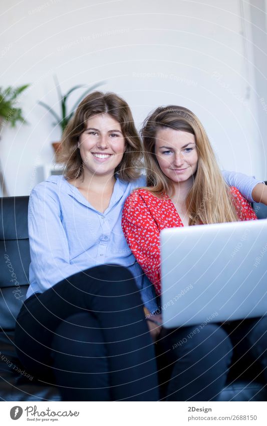 Zwei lächelnde junge Frauen sitzen auf dem Sofa mit Laptop. Lifestyle Glück schön Haus Arbeit & Erwerbstätigkeit Computer Notebook Technik & Technologie