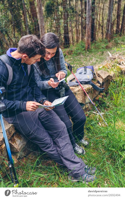 Ein Paar beim Trekking im Sitzen, das mobil aussieht und eine Karte hat. Ausflug Abenteuer Sightseeing Berge u. Gebirge wandern Sport PDA Mensch Frau Erwachsene