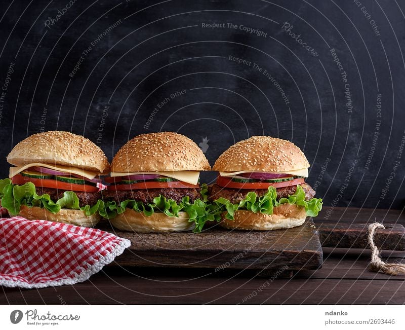 drei Hamburger mit Gemüse Fleisch Käse Brot Brötchen Mittagessen Abendessen Fastfood Tisch Tafel Holz dunkel frisch schwarz Salatbeilage Amerikaner Hintergrund