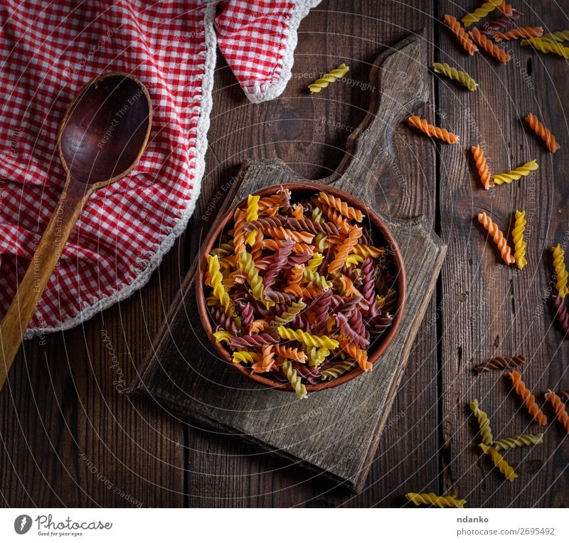 rohe Nudelnusilli auf einem braunen Holztisch Teigwaren Backwaren Ernährung Diät Schalen & Schüsseln Löffel Tisch frisch retro gelb rot Farbe Tradition Top