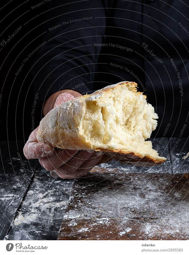 Chefkoch hält halbgebackenes weißes Weizenmehlbrot in der Hand. Brot Ernährung Tisch Küche Mensch Finger Holz machen dunkel frisch braun schwarz Tradition