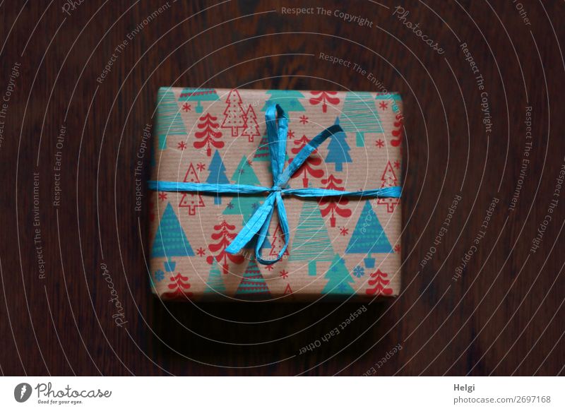 kleines Päckchen als Geschenk verpackt in rot-blau-türkisem  Papier mit Weihnachtsmotiven und türkisfabener Bastschleife Zettel Verpackung