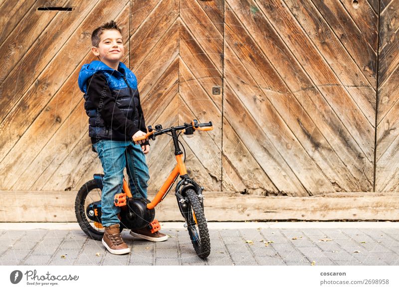 Kleiner Junge mit Fahrrad auf Holztürhintergrund Lifestyle Freude Glück schön Gesicht Freizeit & Hobby Spielen Ferien & Urlaub & Reisen Ausflug Städtereise Haus