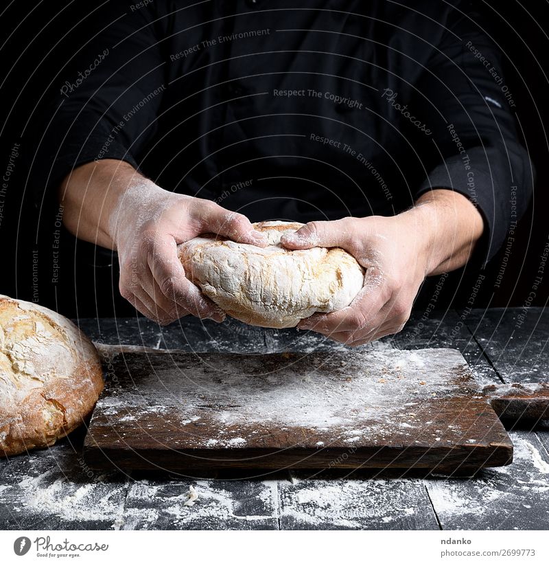 männliche Kochhände halten einen ganzen Laib gebackenes Rundbrot. Brot Ernährung Tisch Küche Mensch Hand machen dunkel frisch braun schwarz weiß Tradition