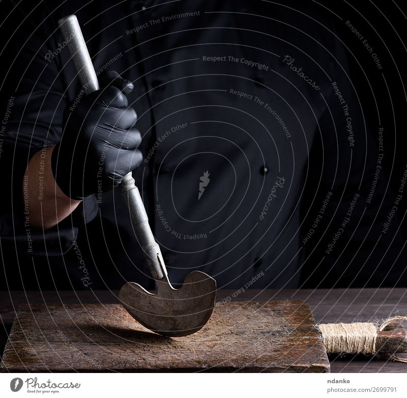 Koch in schwarzer Kleidung hält in der Hand ein altes Metallmesser. Messer Küche Beruf Handschuhe Stahl weiß Holzplatte Hackmesser Metzger Küchenchef Halt