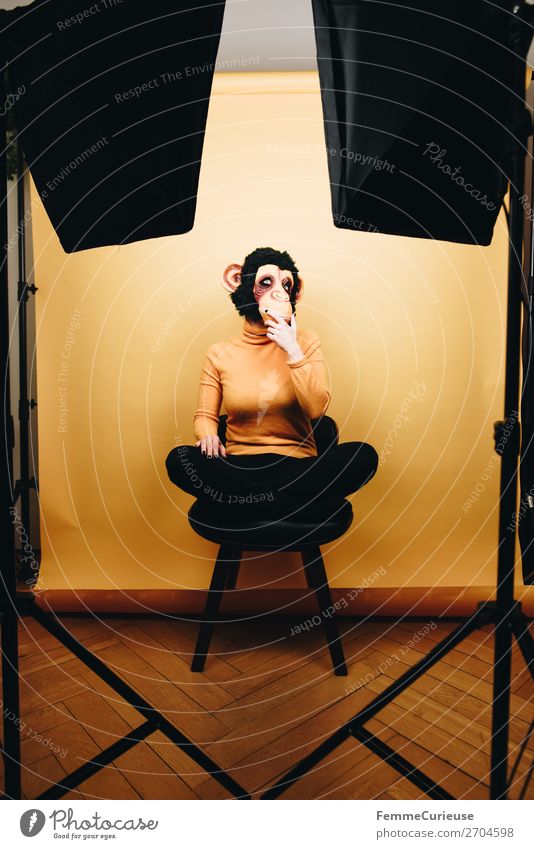 Woman with monkey mask sitting thoughtfully in photo studio feminin Frau Erwachsene 1 Mensch 18-30 Jahre Jugendliche 30-45 Jahre Freude Affen Affenmaske