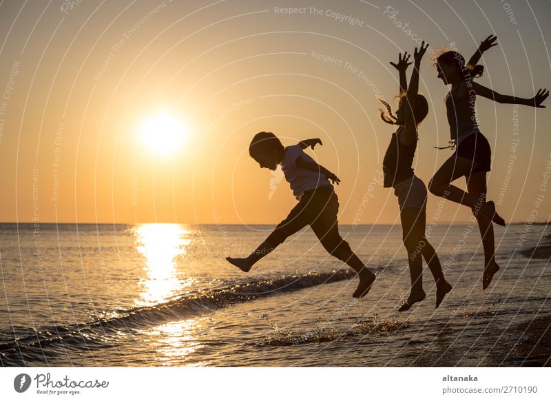 Glückliche Kinder, die zur Zeit des Sonnenuntergangs am Strand spielen. Drei Kinder, die sich im Freien vergnügen. Konzept der Sommerferien und einer freundlichen Familie.