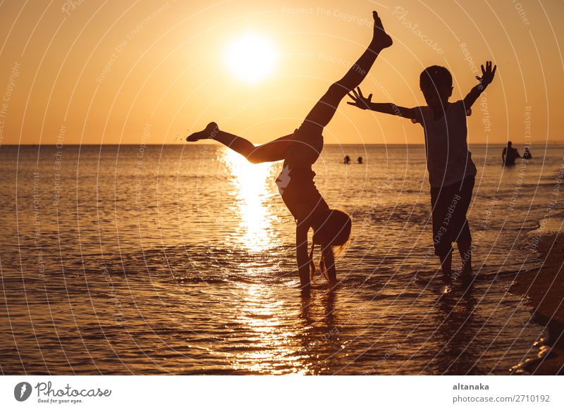 Glückliche Kinder, die zur Zeit des Sonnenuntergangs am Strand spielen. Zwei Kinder, die sich im Freien vergnügen. Konzept der Sommerferien und einer freundlichen Familie.