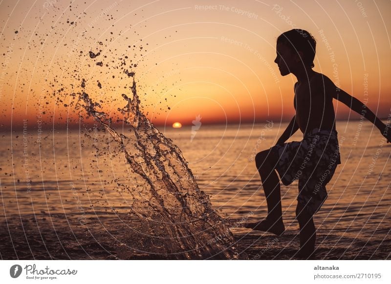 Ein glücklicher kleiner Junge, der zur Zeit des Sonnenuntergangs am Strand spielt. Ein Kind, das Spaß im Freien hat. Konzept der Sommerferien. Lifestyle Freude