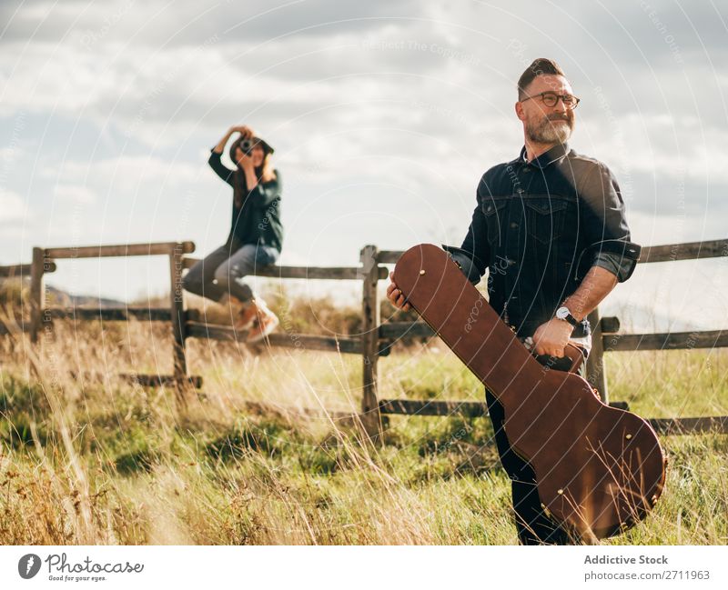 Frau, die mit der Gitarre einen Mann fotografiert. Natur Musiker Fotograf fallen sitzen ländlich Zaun Lifestyle Mensch Sommer lässig akustisch gutaussehend Typ