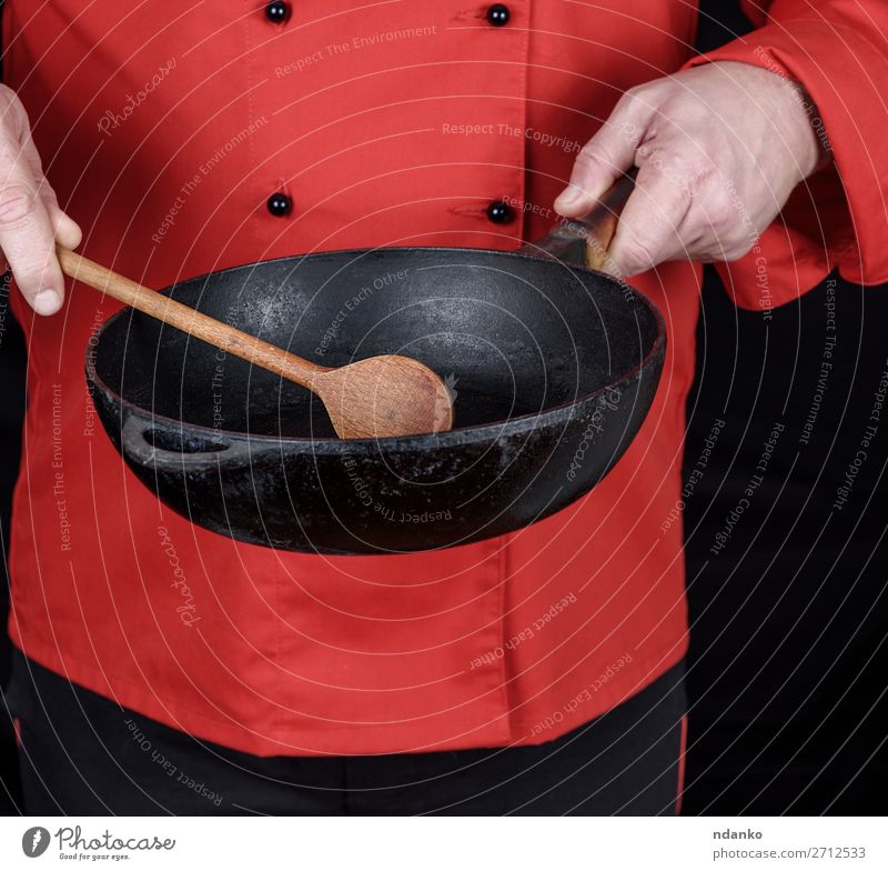 in roter Uniform kochen und eine leere schwarze Bratpfanne halten. Pfanne Löffel Küche Restaurant Beruf Koch Mensch Mann Erwachsene Hand Bekleidung Gußeisen