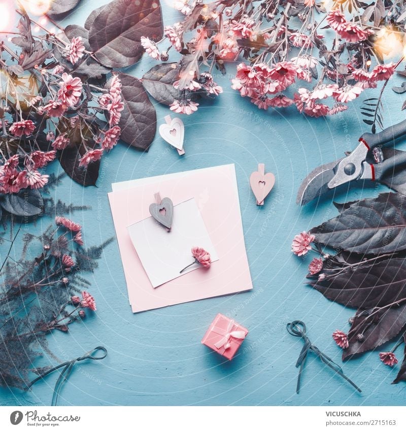 Blanko-Grußkarte auf blauem Floristenschreibtisch mit rosa Blumen, Herzen und Geschenkbox. blanko Blumenhändler Schreibtisch Kasten abstrakt Konzept Muttertag