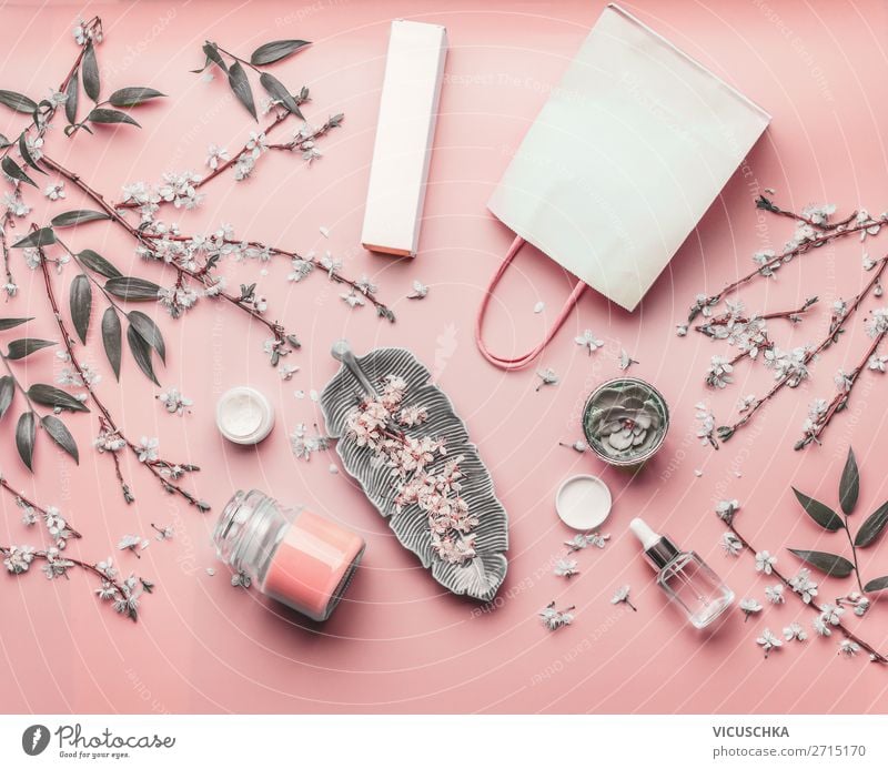 Kosmetisches Konzept. Verschiedene Gesichtsprodukte und Papier-Einkaufstasche auf pastellrosa Hintergrund mit Kirschblüte und Blättern, Draufsicht, Rahmen. Kopieren Sie Platz für Ihren Entwurf. Layout des Schönheitsblogs. Flachbett