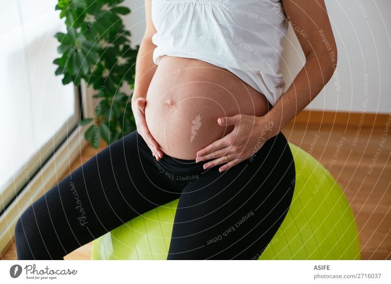Schwangere Frau, die zu Hause trainiert und auf dem Fitball sitzt. Glück Körper Sport Baby Erwachsene Eltern Mutter Hand berühren Fitness sitzen schwanger grün