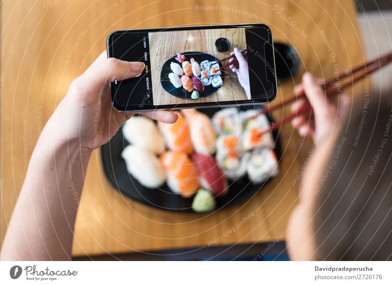 Draufsicht der Frau, die Sushi auf dem Tisch fotografiert. Fotografie PDA Mobile Telefon Schuss Hand Lebensmittel Soja maki Kalifornische Walze Essstäbchen