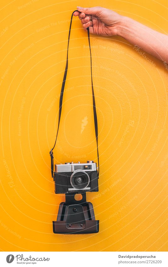 Hand hält eine Vintage-Kamera an der orangefarbenen Wand isoliert. Arme Fotokamera altehrwürdig Orange retro vereinzelt Studioaufnahme Halt Freizeit & Hobby